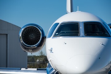 A tight close-up view of business jet's left engine and cockpit from front-left angle under bright...