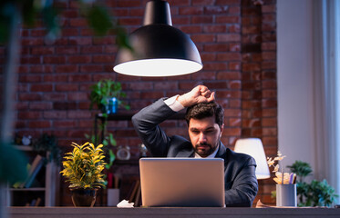 Indian businessman at desk holding head in pain, suffering from stress and workplace burnout