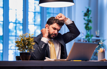 Indian businessman at desk holding head in pain, suffering from stress and workplace burnout