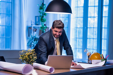Asian architect working on technical drawing and blueprint at office desk with focused expression