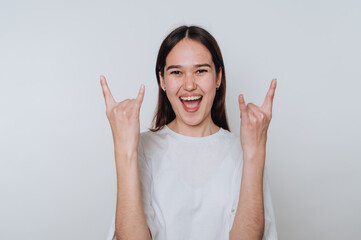 Young asian woman showing rock and roll hand gesture while smiling against a light background