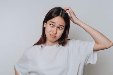 Confusion expressed by a young woman touching her head in casual attire against a neutral background