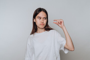 Young asian woman expressing dissatisfaction with a small object in a simple background while...