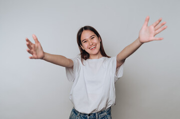 Young asian woman smiling and reaching out with open arms against a plain background in a relaxed...