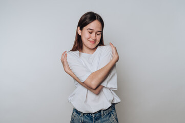 Smiling asian young woman embraces herself in a cozy indoor space during a calm moment