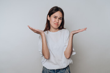 Young woman with a puzzled expression gestures with her hands in a neutral setting during the day