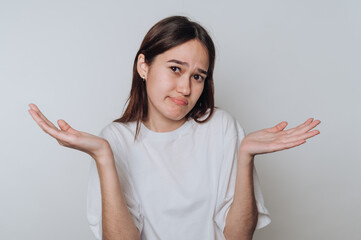 Young asian woman with a puzzled expression gestures with open hands on a plain background during...