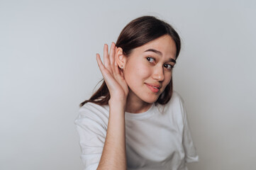 Young asian woman listening intently with a playful expression against a neutral background