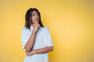 Thoughtful young african american man with braided hair poses against a bright yellow background,...