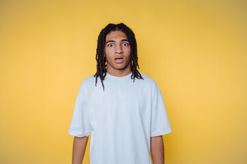 Surprised african young man with long curly hair against a bright yellow background expressing...