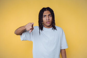 Young person with braided hair expressing surprise while pointing against a bright yellow background