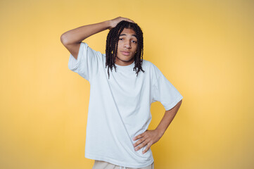 Young man poses with a thoughtful expression against a bright yellow background while wearing...