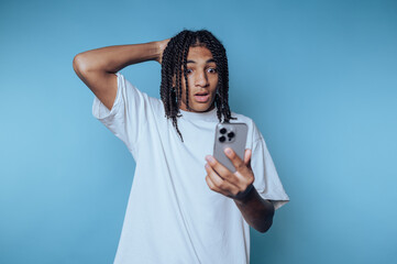 Young individual shows surprise while checking phone against a blue background in a casual setting