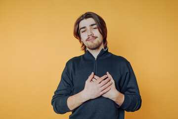 Young man expressing gratitude with hands on heart against bright yellow background indoors