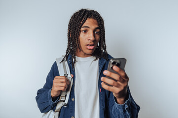 Young man with backpack looks surprised while checking his smartphone in an indoor setting