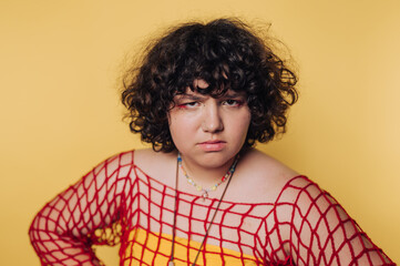 Portrait of an individual wearing a colorful outfit with curly hair posed against a bright yellow...