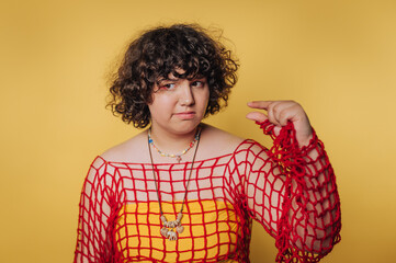 Individual poses confidently wearing a red net top over a yellow outfit against a bright yellow...