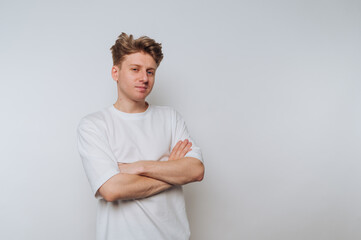 Young man in casual white t-shirt posing with crossed arms against a white background in a well-lit...