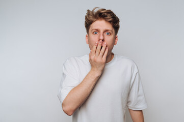Young man showing surprise with hand over mouth in a light-colored setting during a casual moment