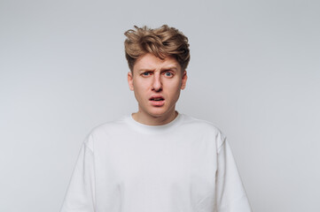 Confused young man with tousled hair standing against a plain backdrop during a casual indoor moment