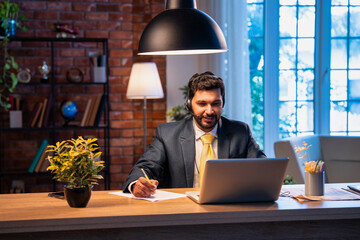 Indian businessman writes notes during online call, showing focus, learning, and remote teamwork