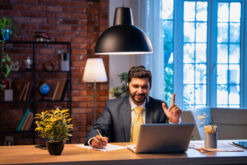 Indian businessman writes notes during online call, showing focus, learning, and remote teamwork