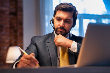 Indian businessman writes notes during online call, showing focus, learning, and remote teamwork