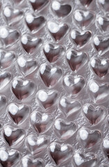 Close-up of heart shaped bubble wrap on a shiny silver background. Plastic texture with a top-down view, ideal for product packaging or commercial design projects. Unique and playful pattern.