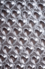 Close-up of heart shaped bubble wrap on a shiny silver background. Plastic texture with a top-down view, ideal for product packaging or commercial design projects. Unique and playful pattern.