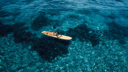 Woman swim on surfboard in blue ocean. Drone view of woman during surfing