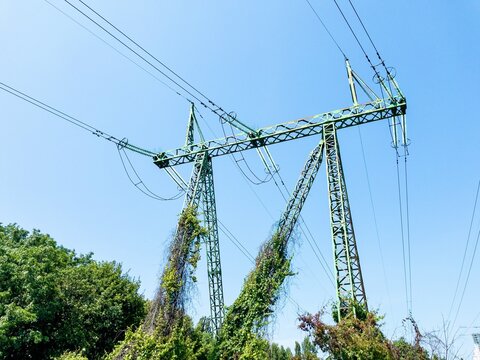 Electric power transmission towers with high-voltage lines against clear blue sky, metal lattice structures for energy distribution, industrial infrastructure in outdoor urban environment