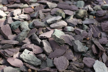 Close-up of natural slate rocks in purple and green tones, with light and shadow crossing the surface to highlight their texture and layered form.