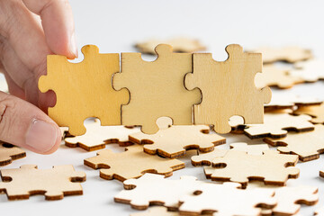 hand holding wooden jigsaw puzzle pieces. with scattered puzzle pieces in background.