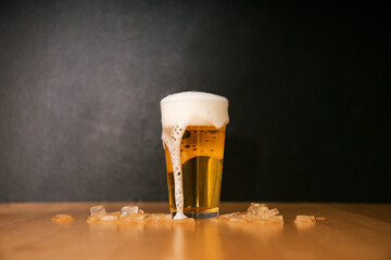 Overflowing Glass of Cold Beer with Foam and Ice on Wooden Table