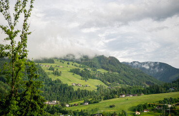 Obraz premium Misty morning over green alpine valley with scattered houses in Austrian countryside