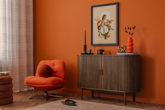Bright and modern interior with an orange armchair, mock up art print, eclectic accessories styled on a dark wood cabinet. A bold and graphic setup.