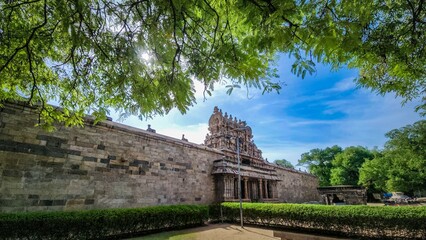 Ancient South Indian temple gopuram framed by lush greenery under a vibrant blue sky – a serene...