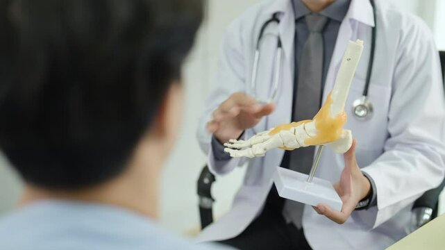 Doctor explaining foot joint anatomy to patient using realistic bone model during orthopedic consultation, healthcare professional demonstrating bone structure and discussing foot or ankle condition.