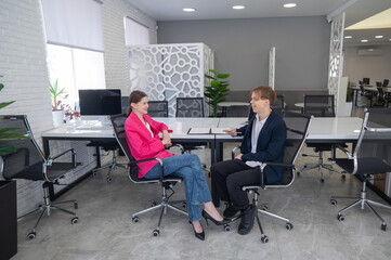Man and woman talking while sitting at desk in office. 
