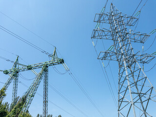Electric power transmission towers with high-voltage lines against clear blue sky, metal lattice...