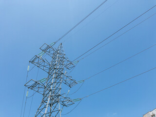Electric power transmission towers with high-voltage lines against clear blue sky, metal lattice...