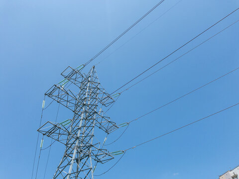 Electric power transmission towers with high-voltage lines against clear blue sky, metal lattice structures for energy distribution, industrial infrastructure in outdoor urban environment