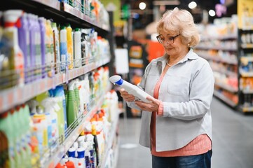 Elderly woman buying household chemicals or laundry detergent at supermarket.