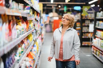 Mature female shopper buying laundry detergent in household chemicals store