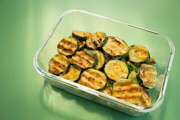 Fried zucchini slices on a glass bowl on a green background