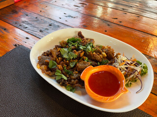 Fried beef with chili sauce on a white plate on a wooden table