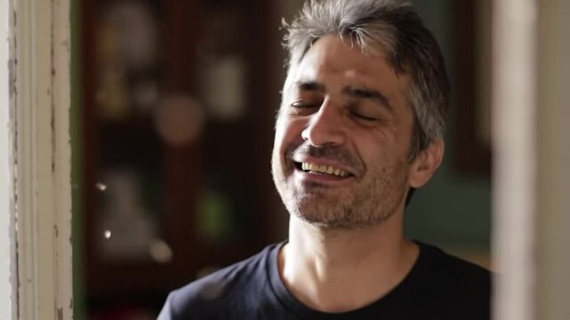 Man closing his eyes and smiling as breeze passes through an open window