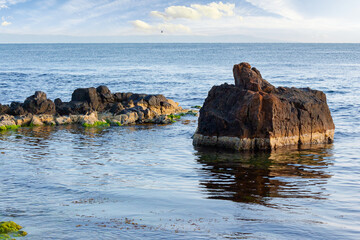seascape with rock in the water. textured boulder reflecting calm sea surface in morning light....