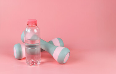 pink bottle of water and two dumbbells isolated on pink background. Health and fitness concept.