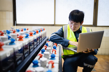 Technician inspects battery backup system using laptop to ensure power supply and maintenance are...